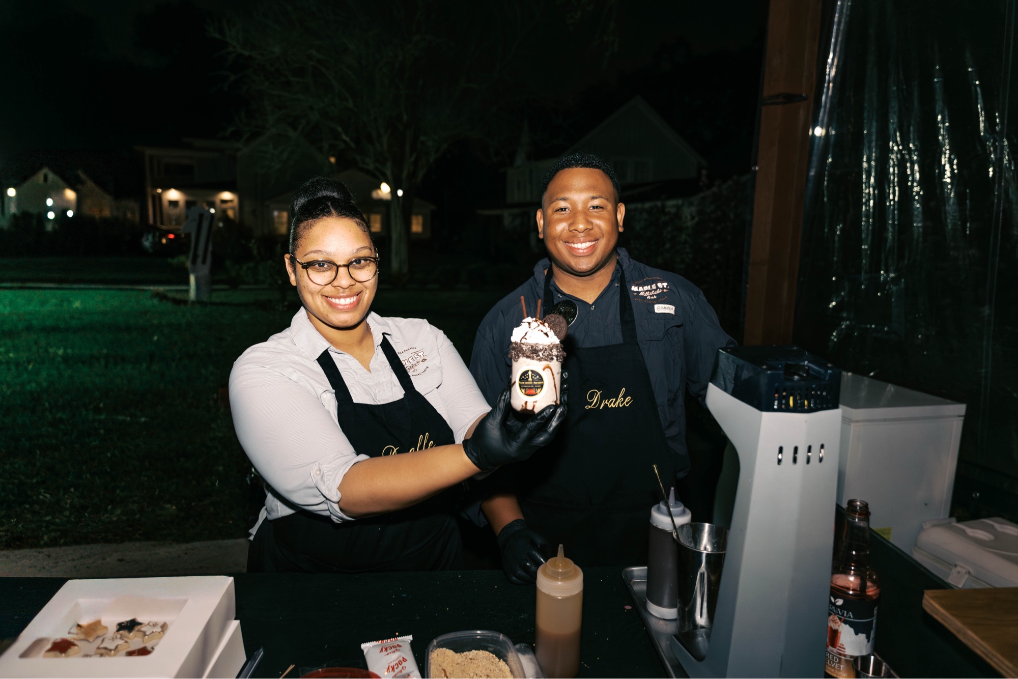 Drake and Danielle of Maple Street Milkshake Bar at an evening pop-up, presenting a hand-crafted Chocolate Avalanche milkshake.